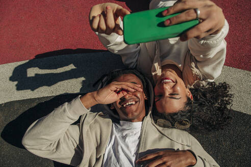 Glückliche junge Freunde nehmen Selfie durch Smartphone, während in Spielplatz liegen - MASF31351