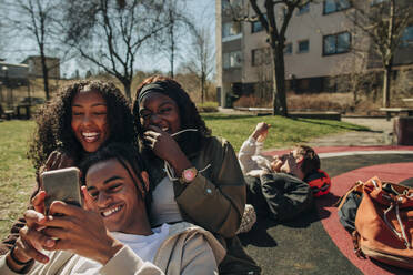 Glückliche junge Freunde teilen Smartphone zusammen auf dem Spielplatz an einem sonnigen Tag - MASF31356