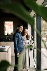 Gut gelaunte Kunden, die durch das Fenster schauen, während sie in ihrem neuen Zuhause stehen - MASF31379