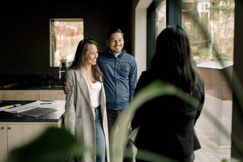 Smiling couple with salesperson standing by window in kitchen - MASF31386