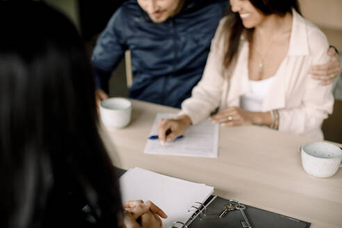 Real estate agent with couple signing contract at table in new house - MASF31393