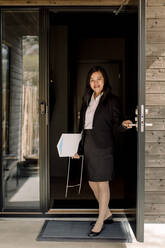 Porträt eines lächelnden Immobilienmaklers, der die Tür am Eingang eines neuen Hauses öffnet - MASF31397