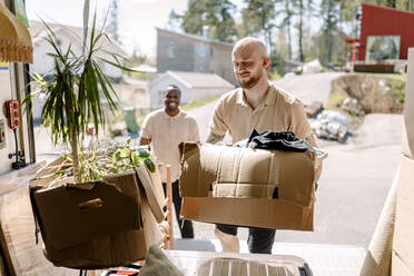 Multiracial movers carrying boxes from truck during sunny day - MASF31406