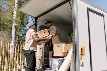 Multirassische Umzugshelfer entladen an einem sonnigen Tag Kartons vom Lastwagen - MASF31412