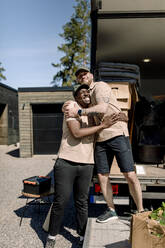 Glückliche Lieferanten, die sich umarmen, während sie vor einem Lastwagen stehen - MASF31419