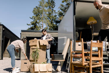 Couple opening cardboard boxes while delivery man unloading furniture from truck - MASF31428