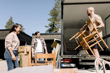 Ein Ehepaar sieht zu, wie ein Möbelpacker an einem sonnigen Tag Stühle vom Lastwagen ablädt - MASF31430