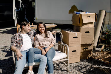 Lächelndes Paar, das auf einem Stuhl sitzt, während es in ein neues Haus umzieht - MASF31434
