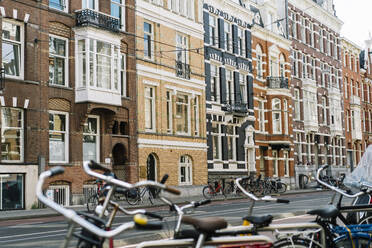 Fassaden verschiedener typischer Wohngebäude aus Backstein mit weißen Fenstern und Balkonen in einer Stadt mit Fahrrädern, die auf Gehwegen in der Nähe einer asphaltierten Straße in den Niederlanden abgestellt sind - ADSF35497