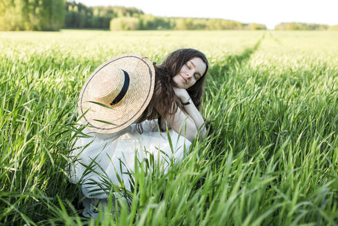 Smiling woman with eyes closed crouching on field - LLUF00715