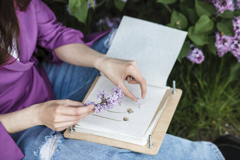 Frau sitzend mit fliederfarbener Blume und Buch - LLUF00719