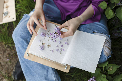 Frau mit fliederfarbenen Blumen und einem Buch sitzend - LLUF00721