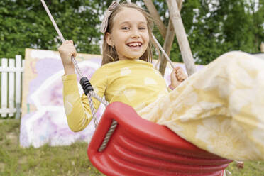 Smiling girl swinging on swing at playground - KMKF01860