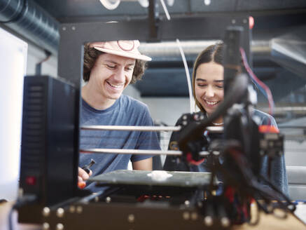 Lächelnde Ingenieure bei der Arbeit mit einem 3D-Drucker in einer Werkstatt - CVF01994