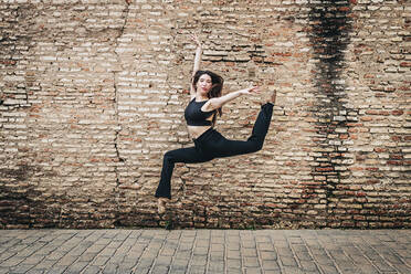 Young ballet dancer dancing in front of brick wall - JRVF02960