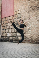 Woman practicing ballet near brick wall - JRVF02962