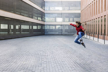 Man with arms outstretched jumping in front of building - XLGF02954