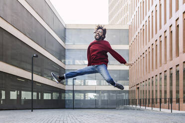 Cheerful man jumping in front of building - XLGF02955