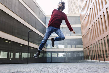 Smiling man jumping over street - XLGF02956