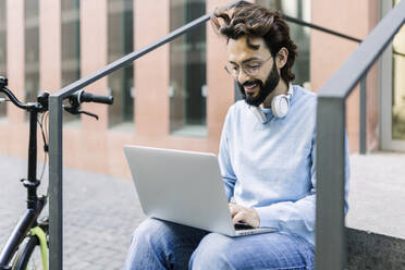 Freelancer using laptop sitting by railing - XLGF02960