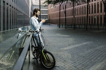 Lächelnder Mann mit Mobiltelefon auf der Straße - XLGF02967