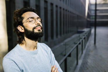 Bearded man with eyes closed in front of building - XLGF02969