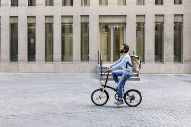 Mann mit Rucksack auf dem Fahrrad in der Stadt - XLGF02972