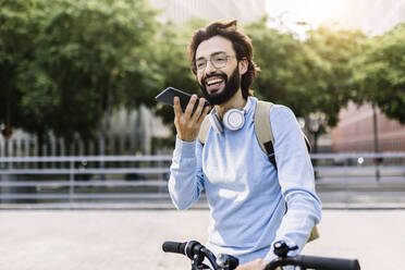 Lächelnder Mann mit drahtlosen Kopfhörern, der über einen Lautsprecher telefoniert - XLGF02988