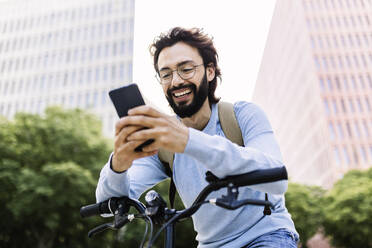 Smiling man using mobile phone leaning on bicycle - XLGF02991
