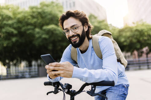 Glücklicher Mann, der ein Smartphone benutzt und sich auf ein Fahrrad stützt - XLGF02992