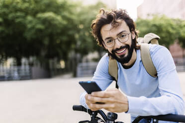 Smiling man with bicycle using mobile phone - XLGF02993