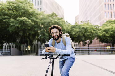 Glücklicher Mann mit Fahrrad, der im Park ein Mobiltelefon benutzt - XLGF02994