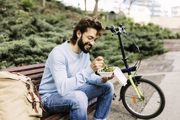 Glücklicher Mann mit Essen auf einer Bank sitzend - XLGF02996