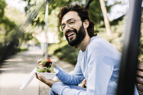 Glücklicher bärtiger Mann mit Salat im Park sitzend - XLGF02998