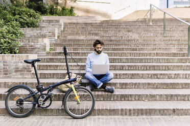 Freiberufler mit Laptop auf den Stufen neben dem Fahrrad sitzend - XLGF03005