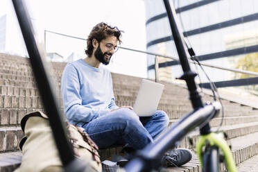 Smiling freelancer using laptop sitting on steps - XLGF03006