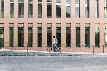 Mann fährt mit dem Fahrrad an einem Gebäude vorbei - XLGF03014