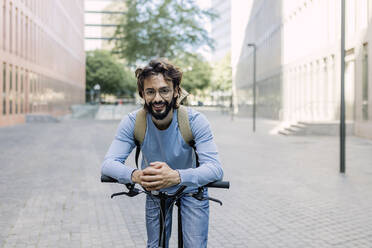 Bearded man with hands clasped leaning on bicycle - XLGF03019