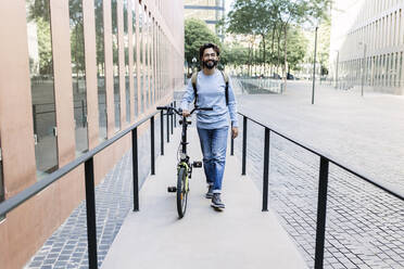 Man with bicycle walking on sidewalk in city - XLGF03021