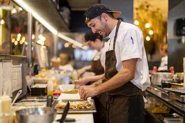 Lächelnder Koch bei der Zubereitung von Speisen in der Restaurantküche - DLTSF02987