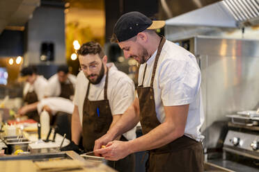 Koch bei der Zubereitung von Speisen neben einem Kollegen in der Restaurantküche - DLTSF02992