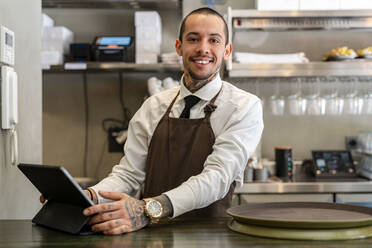 Lächelnder Barkeeper mit Tablet-PC am Bartresen stehend - DLTSF03000