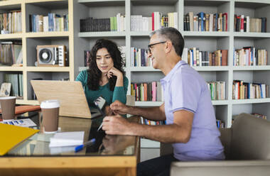 Happy mature businessman with colleague discussing over laptop - JCICF00155