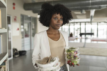 Young businesswoman with salad boxes standing in office - JCICF00173