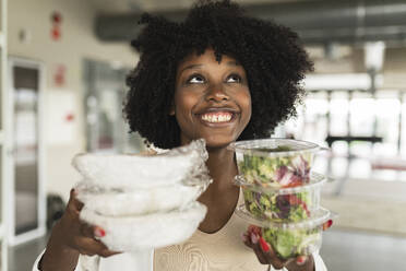 Happy young businesswoman with salad boxes in office - JCICF00175