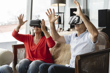 Glückliche Geschäftskollegen, die einen Virtual-Reality-Simulator tragen und auf dem Sofa sitzen und im Büro gestikulieren - JCICF00200