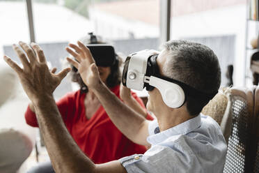 Business colleagues wearing virtual reality simulator gesturing in workplace - JCICF00202