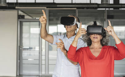 Businesswoman and businessman wearing virtual reality simulator gesturing in office - JCICF00205