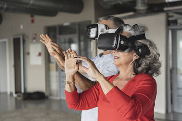 Glückliche Geschäftsfrau mit einem Kollegen, der im Virtual-Reality-Simulator gestikuliert - JCICF00207