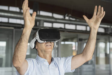 Mature businessman wearing virtual reality simulator gesturing in office - JCICF00214